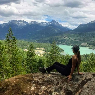 picture of a woman sitting on a rock looking out on mountains, trees and a lake in Whistler BC Canada